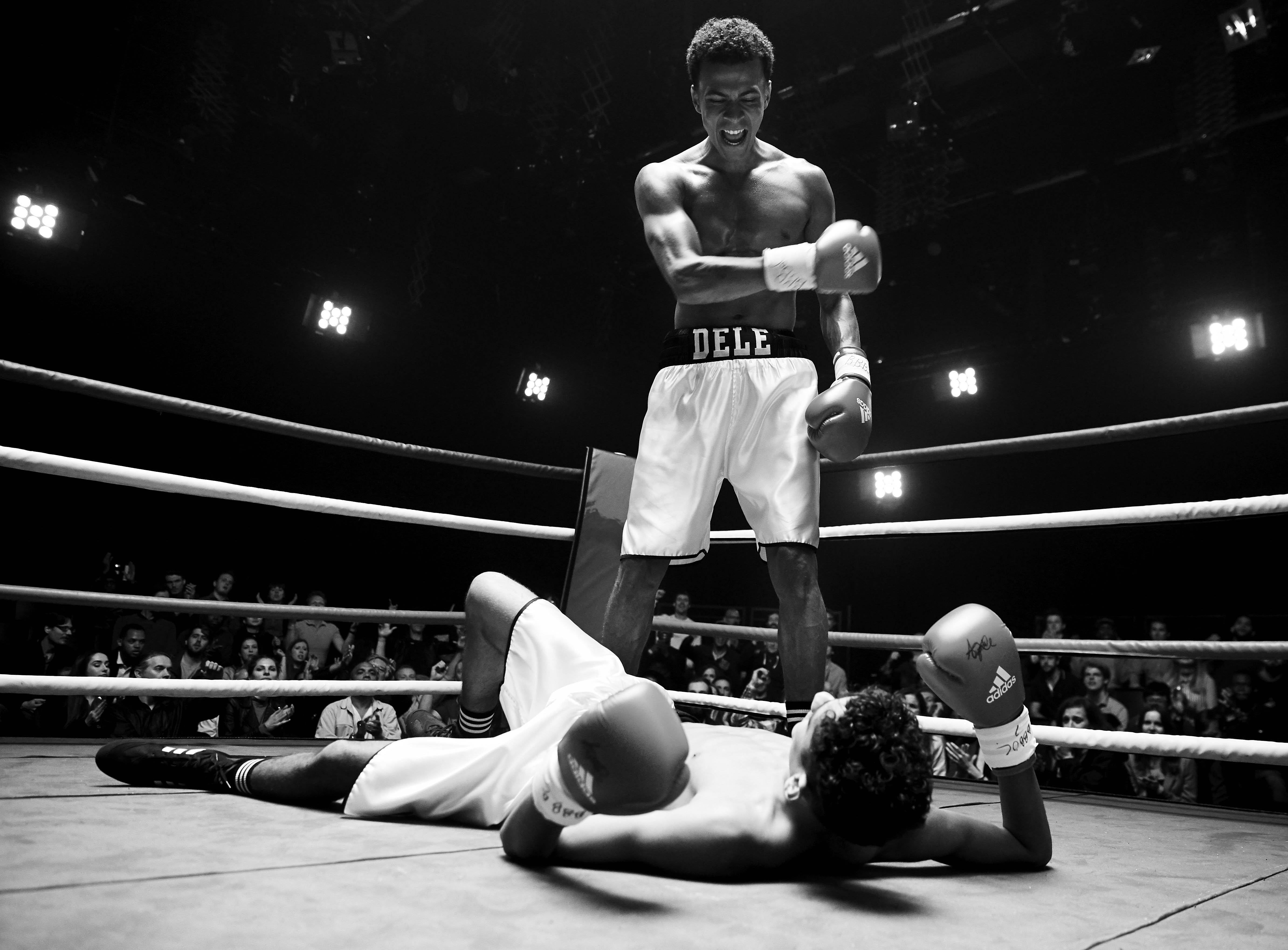 Black and white photo of a boxer standing over a fallen opponent in a boxing ring.