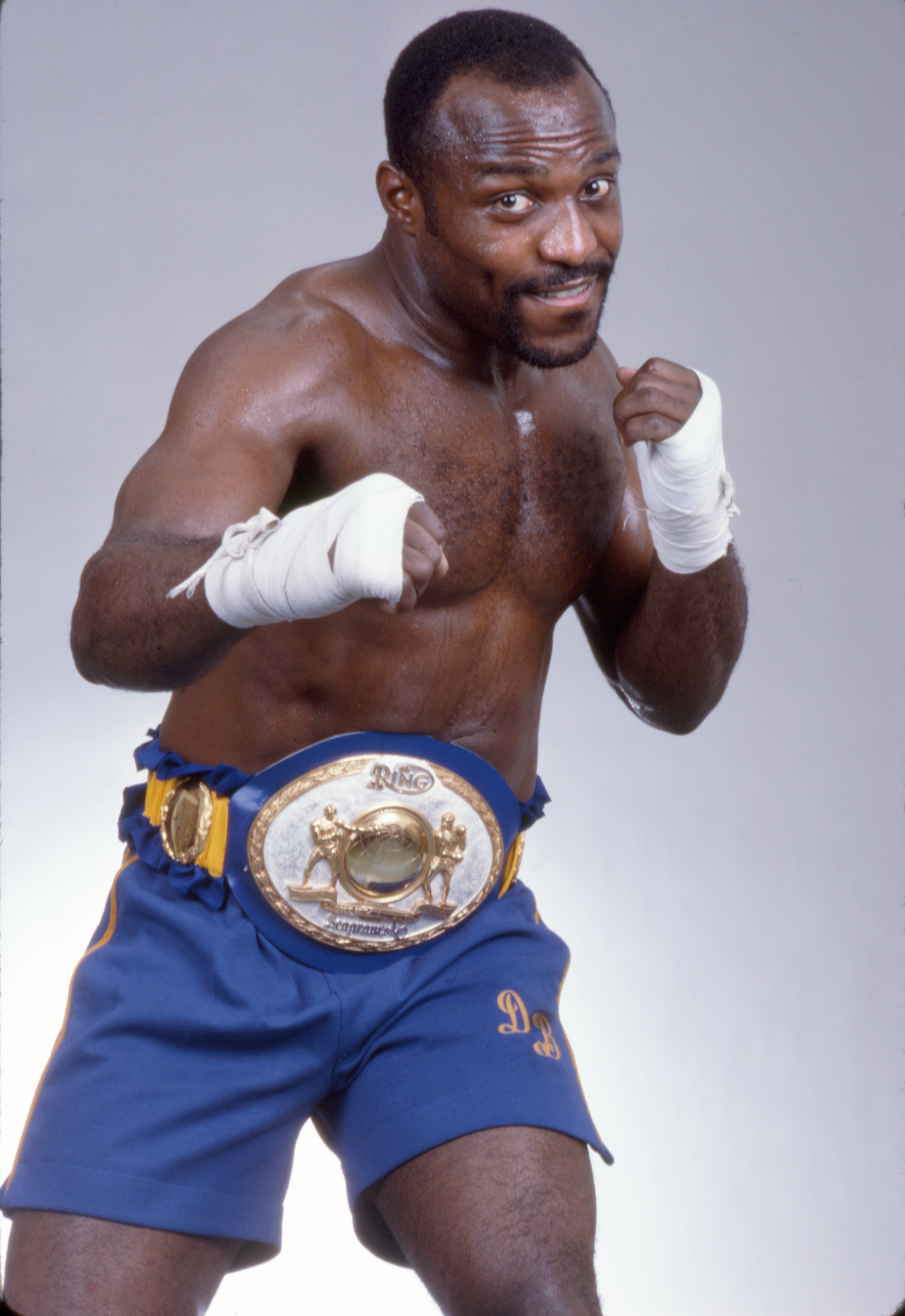 Portrait of Dwight Muhammad Qawi, boxing champion, in a fighting stance wearing his championship belt.