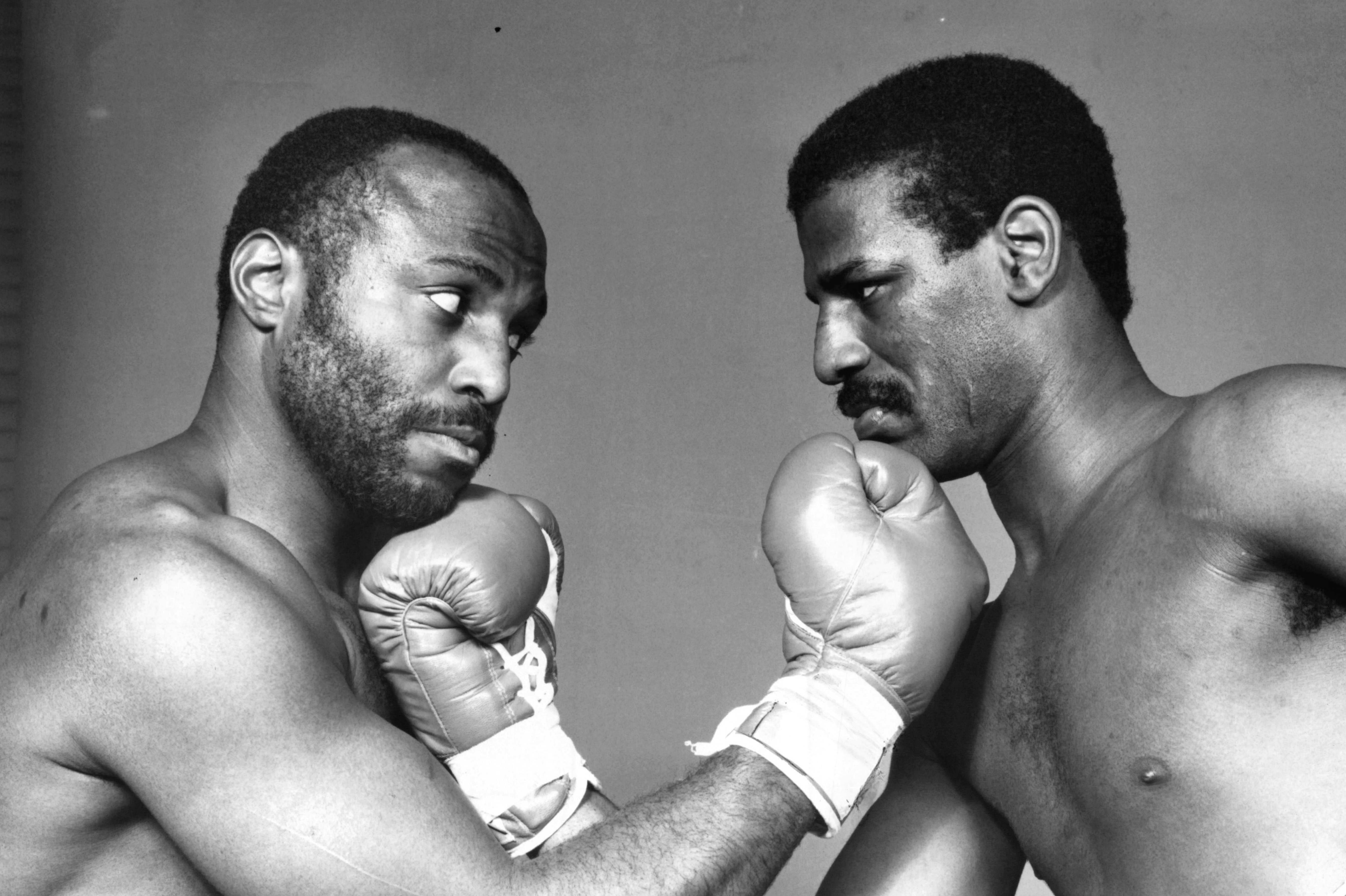 Michael Spinks and Dwight Muhammad Qawi in boxing gloves, facing each other.