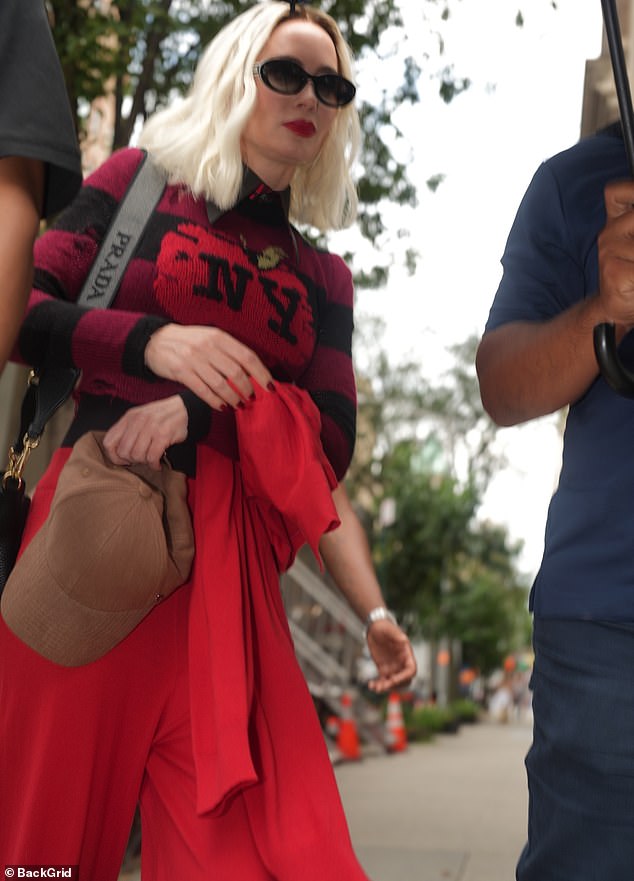 A stylish jacket that matched the slacks was slung over one of Emily's shoulders, and she augmented the outfit with a handbag and a camel-toned baseball cap