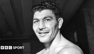 Boxer Jack Gardner punching Johnny Williams in the face, causing him to lean back on to the ropes of the boxing ring.