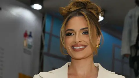 Frennie Shivambu/Gallo Images/Getty Images Mia le Roux smiles whilst wearing a white blazer, gold earrings and her hair in a up-do - Friday 15 August 2025.