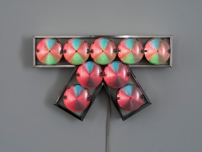 A light sculpture resembling a bow that consists of aluminum, light bulbs, and plastic laminate. 