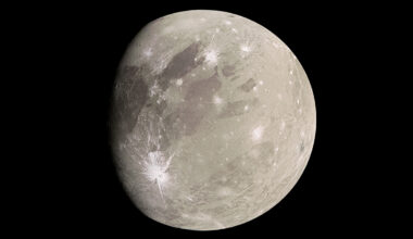 A light tan world marked with bright white craters from meteor impacts