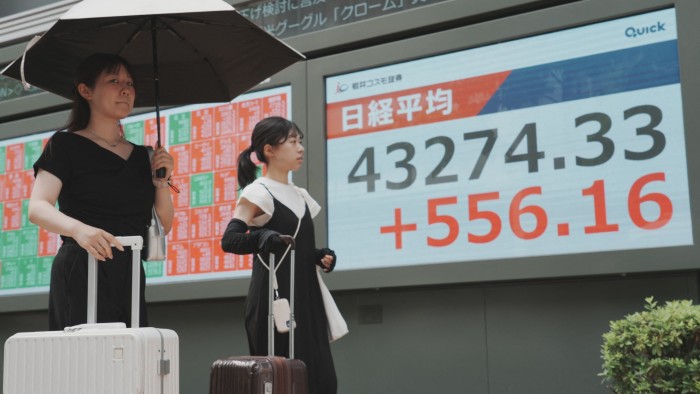 Pedestrians walk in front of an electronic quotation board displaying the Nikkei Stock Average