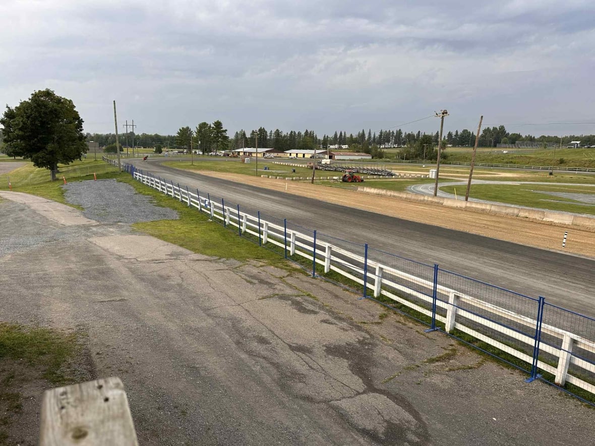 A horse race track with blue metal fencing next to a white wooden fence.