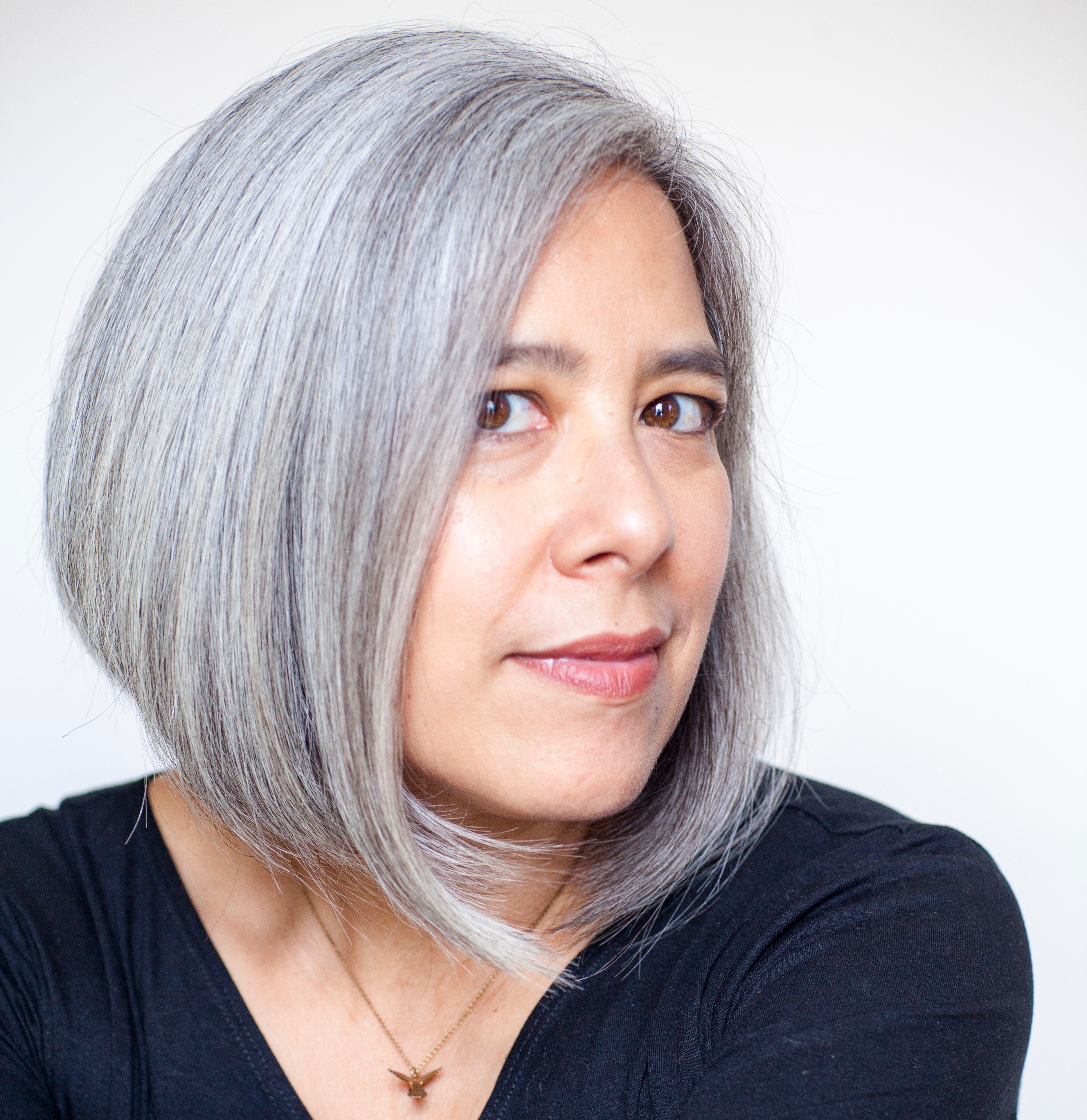 Portrait of author Susan Choi, a woman with gray hair wearing a black shirt and a hummingbird necklace.