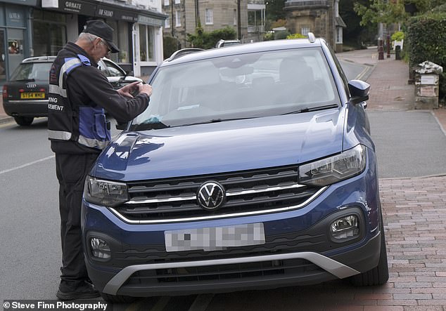 Motorists in Royal Tunbridge Wells, Kent, instead of enjoying the supposed peace and quiet of the garden of England, are 'at war' over what they dub a 'car parking crisis'. Pictured: A traffic enforcement officer placing a ticket on a vehicle in the town this weekend