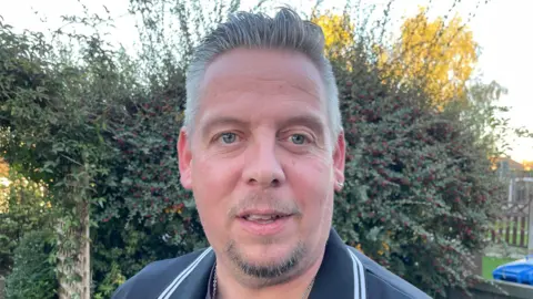 Steve Beech/BBC Man with goatee beard in dark shirt in front of a hedge