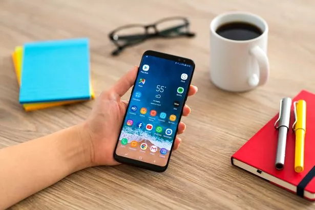 Hand holding a smart phone on a wooden desk. 