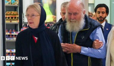 Older British couple Peter and Barbie Reynolds, who were released from Taliban detention in Afghanistan, walking through arrivals at Heathrow Airport. Barbie is wearing deep blue headscarf and dress, a bearded Peter is wearing a blue shirt and dark blue bodywarmer.