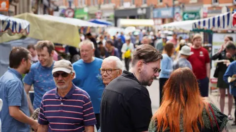 Moseley Farmers' Market A general view image of the market with crowds of people walking around the market with stalls lining both sides of the street. 