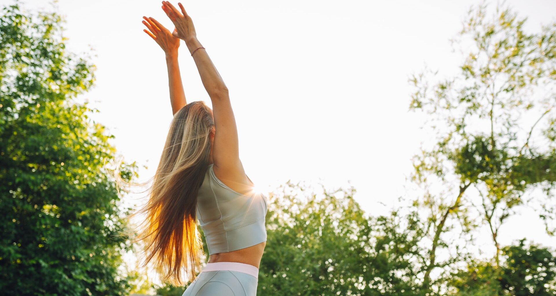 Woman doing wall angels in the garden wearing activewear among trees and sunshine
