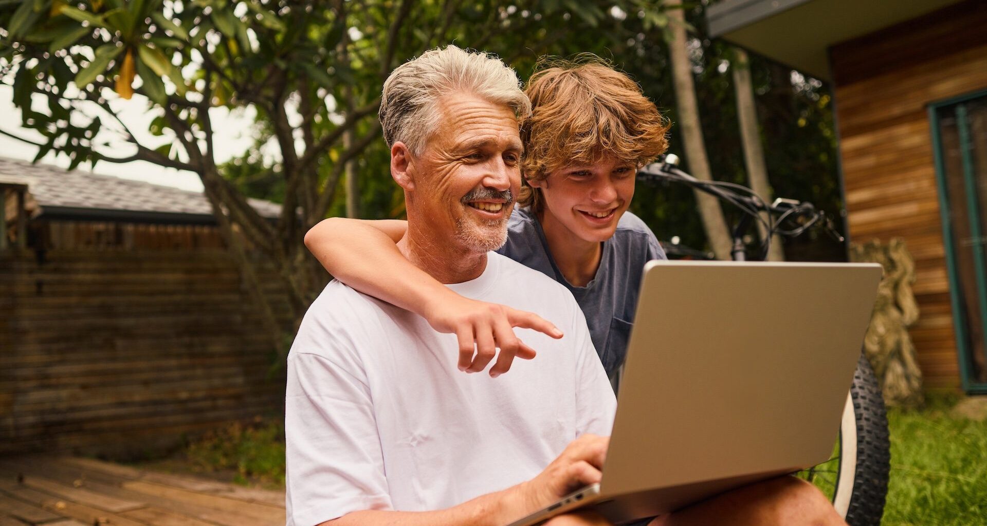 A father and his teenage son looking at a laptop and smiling.