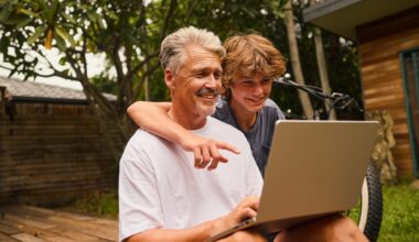 A father and his teenage son looking at a laptop and smiling.