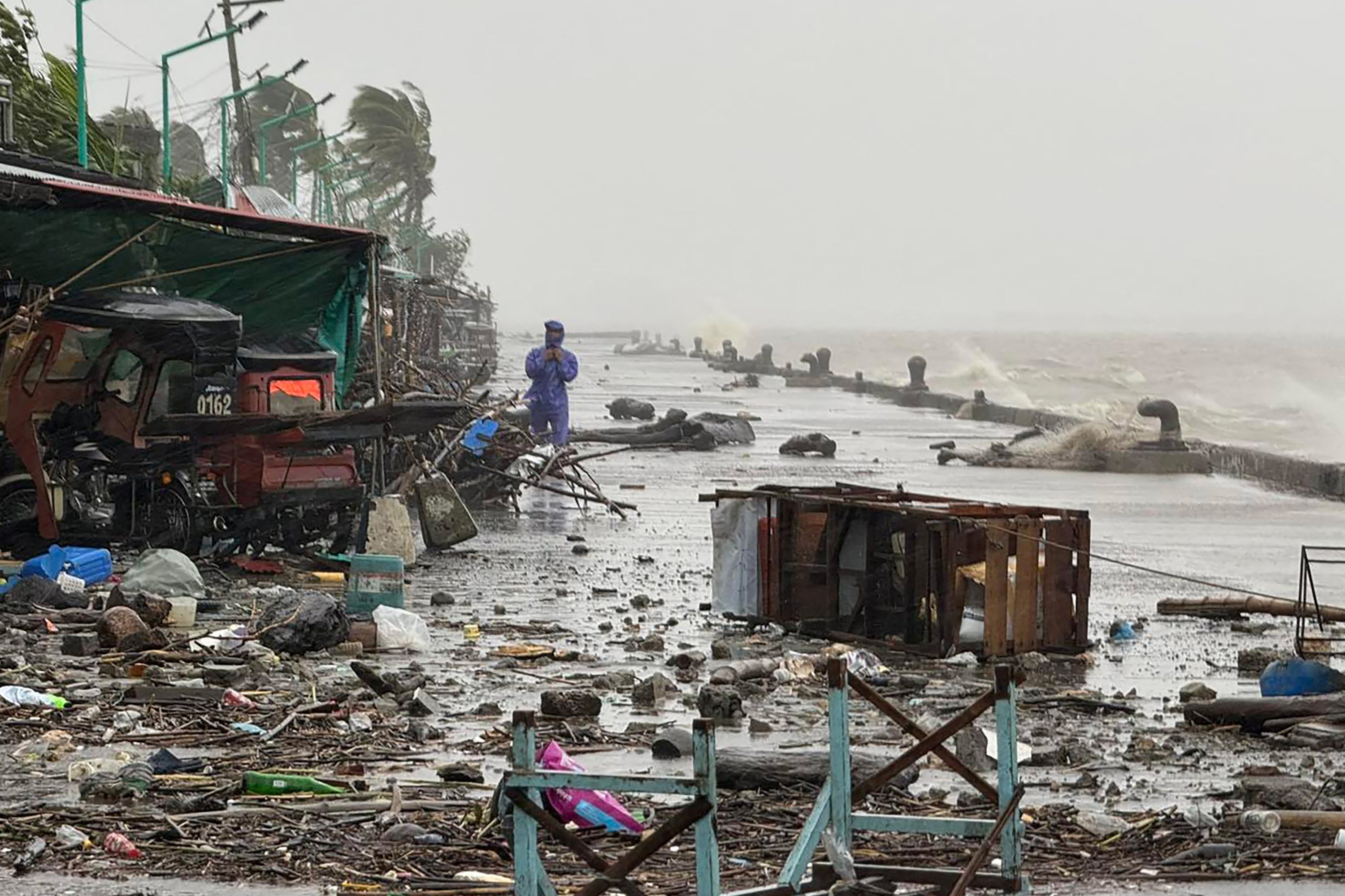 A man stands near debris on a waterfront road amid heavy rain due to weather patterns from Super Typhoon Ragasa in Aparri town, Cagayan province