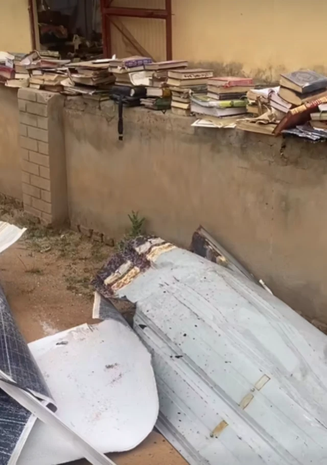 A screenshot of the aftermath of the attack video, parts of the mosque roof are visible on the ground. On a nearby wall there are dozens of books piled on top of one another