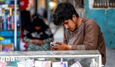 A man sitting at a money exchange stall playing on his phone.