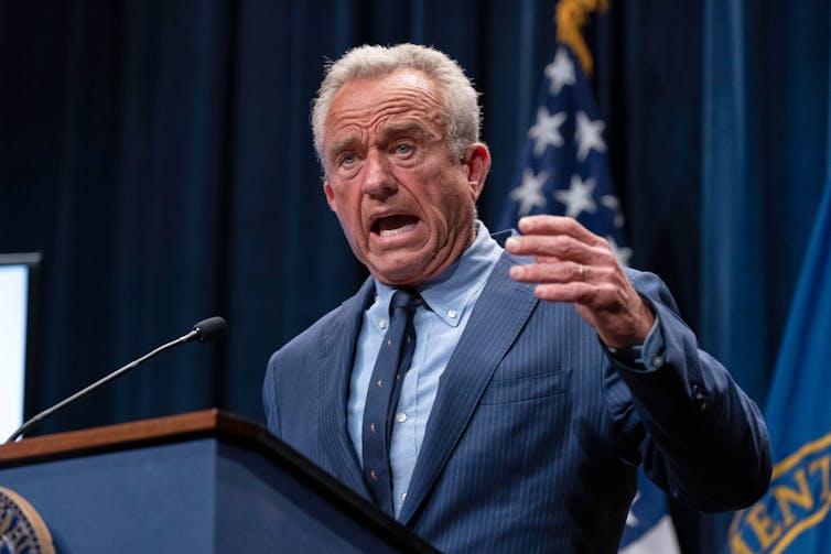 A man with grey hair wearing a blue suit speaking at a podium