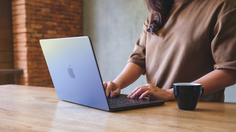 Woman standing at wooden table using gray MacBook