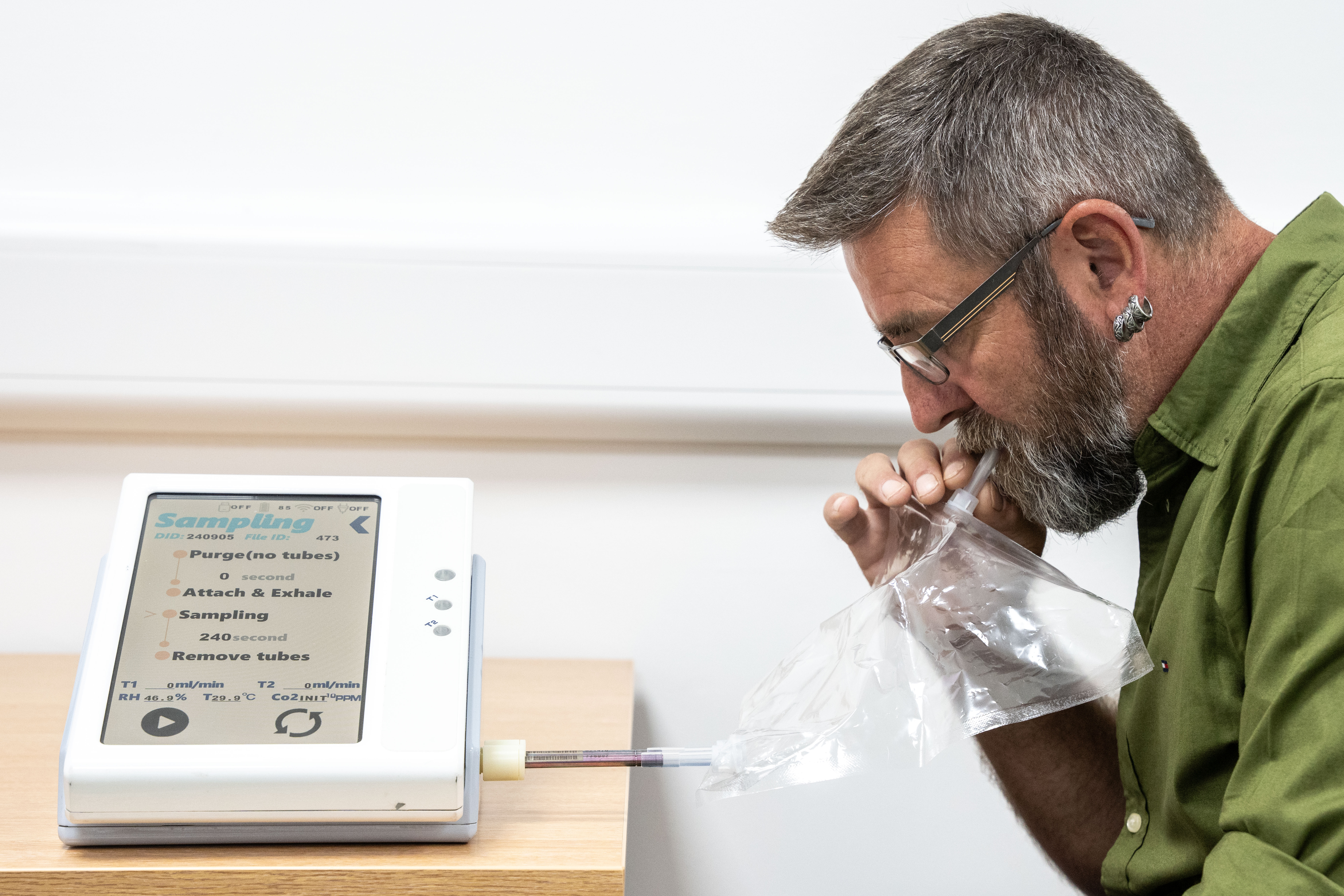 A man taking a breath test for pancreatic cancer by exhaling into a plastic bag connected to a sampling device.