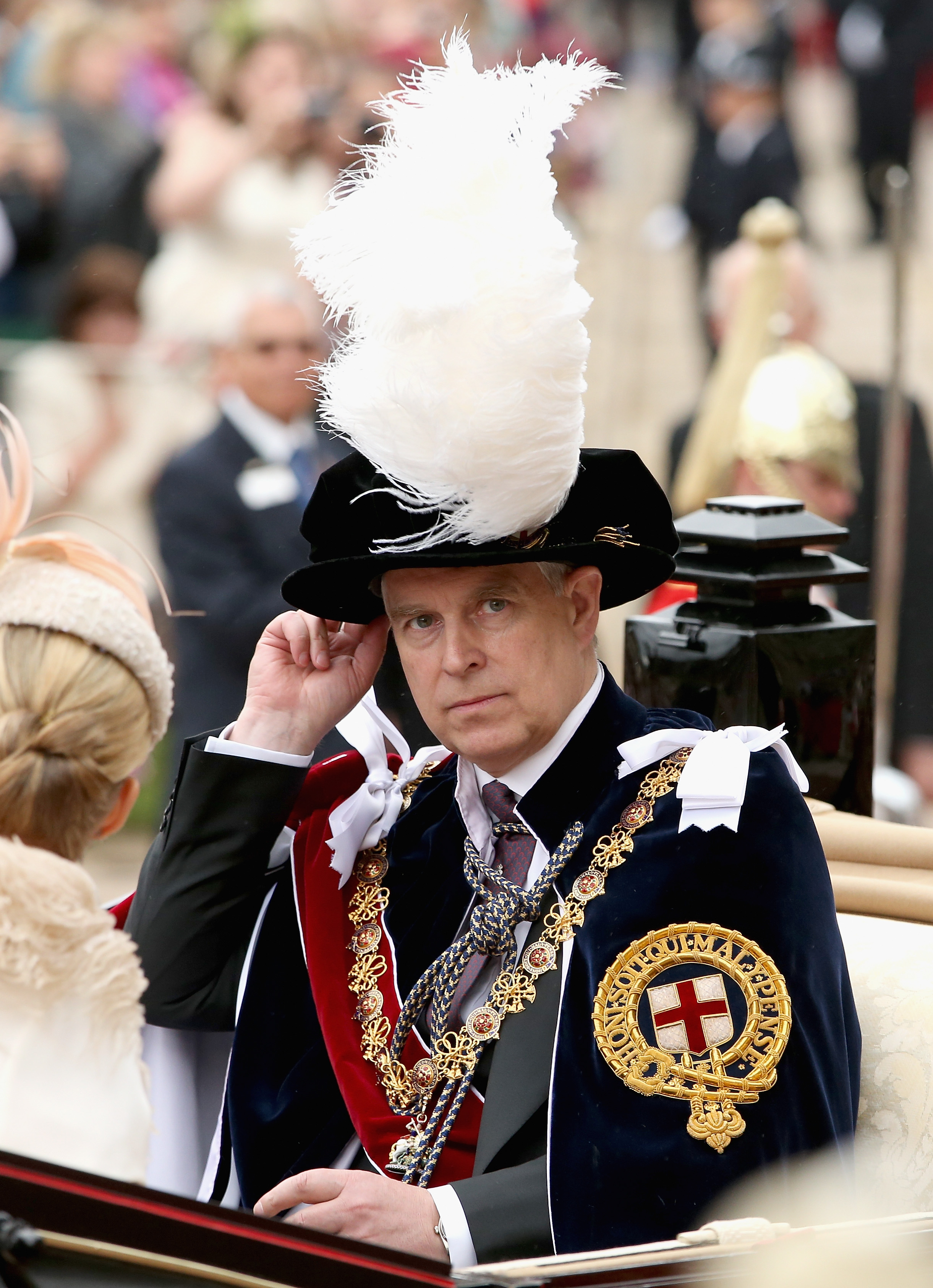 Prince Andrew, Duke of York, in formal ceremonial attire with a plumed hat, traveling in a carriage.