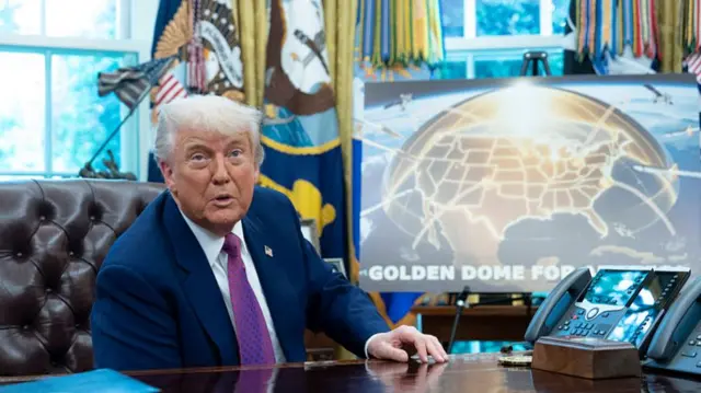Donald Trump sits in a brown leather chair at his desk in the Oval Office. In the background is a gold graphic of the United States, underneath a golden dome. In white capital letters is the caption: 'Golden dome for America'