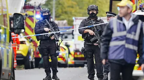 PA Media Armed police at the scene, with police vehicles in the background