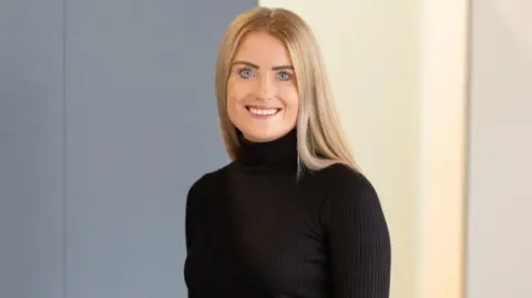 PA Media A caucasian girl in her 20s with long blonde hair and blue eyes smiles at the camera in a professional head-shot whilst wearing a black turtle-neck sweater.