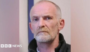 Man with shaved head and goatee beard wearing coat