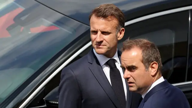 both are standing next to a black car, and are wearing black blazers and white shirts