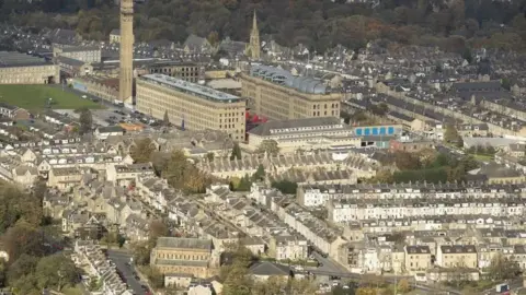 PA Media An aerial view of Bradford city centre - showing the town hall, many houses and buildings and trees in the background.