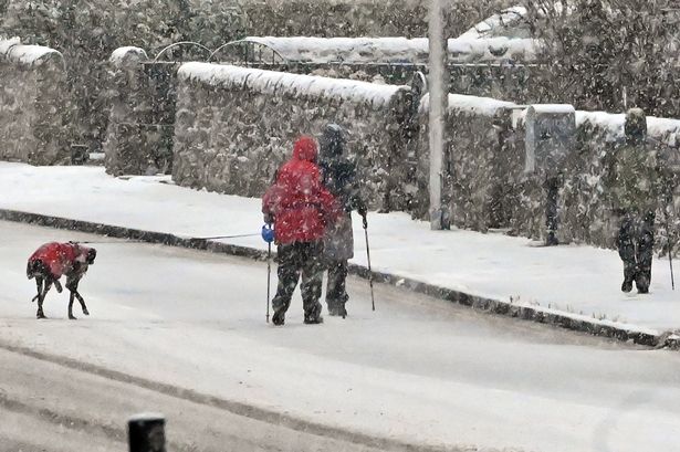 People walk through falling snow on Lanark Road, as wintry conditions close in on the city, on January 5, 2025, in Edinburgh, Scotland. 