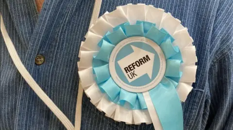 BBC A close-up picture of a Reform UK rosette on a blue denim shirt.