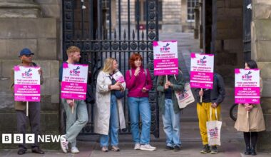 Sanskrity is standing in front of a busy hall. She is wearing a white dress and is looking determinedly at the camera