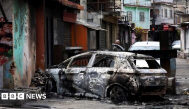A person looks on behind a burnt car during a police operation against drug trafficking at the favela do Penha, in Rio de Janeiro
