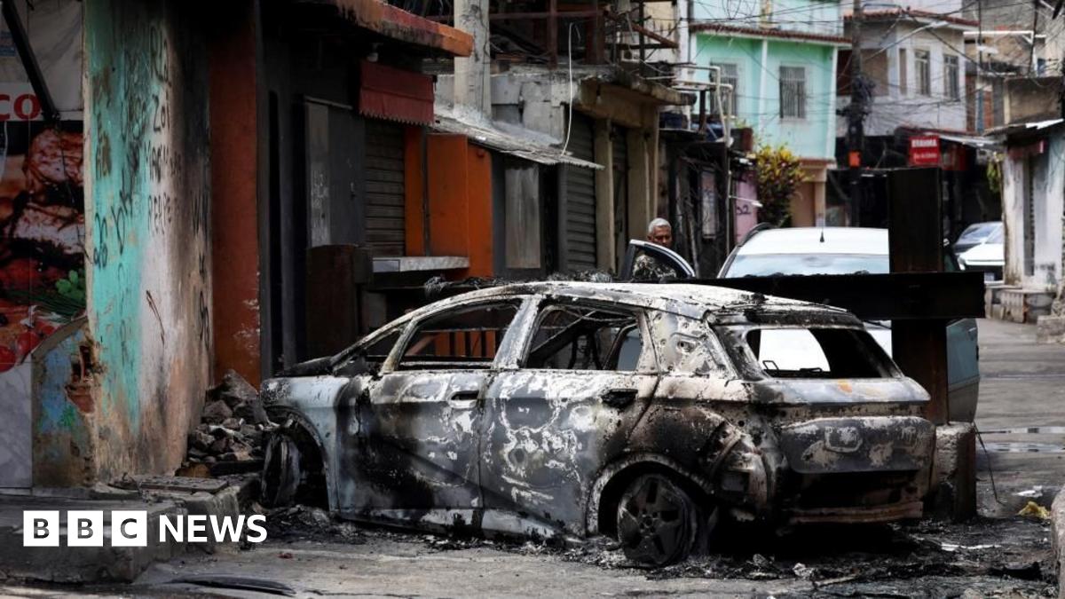 A person looks on behind a burnt car during a police operation against drug trafficking at the favela do Penha, in Rio de Janeiro