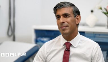 Mr Sunak sits in a hospital chair, wearing a white shirt and burgundy tie.