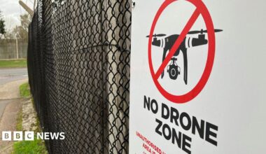 A sign reading 'no drone zone' hanging on a fence at a military base