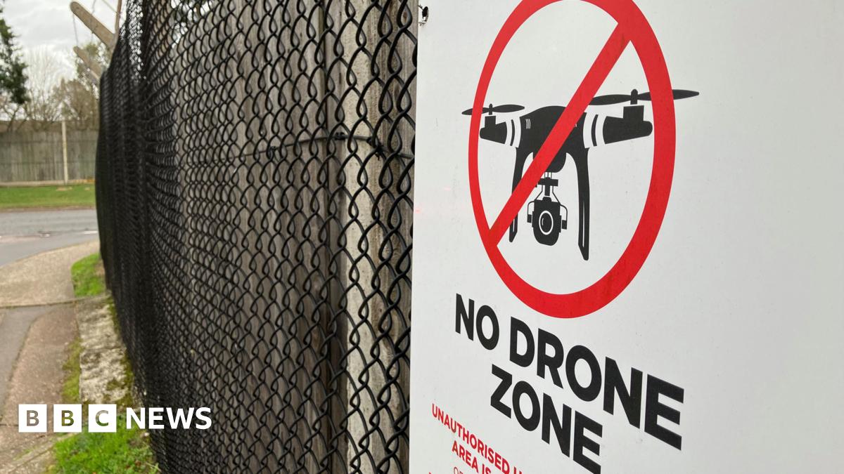 A sign reading 'no drone zone' hanging on a fence at a military base