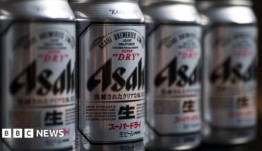 Four silver cans of Asahi beer displayed on a shelf