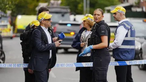 PA Media A police woman is shown along with security staff near a police cordon across a street