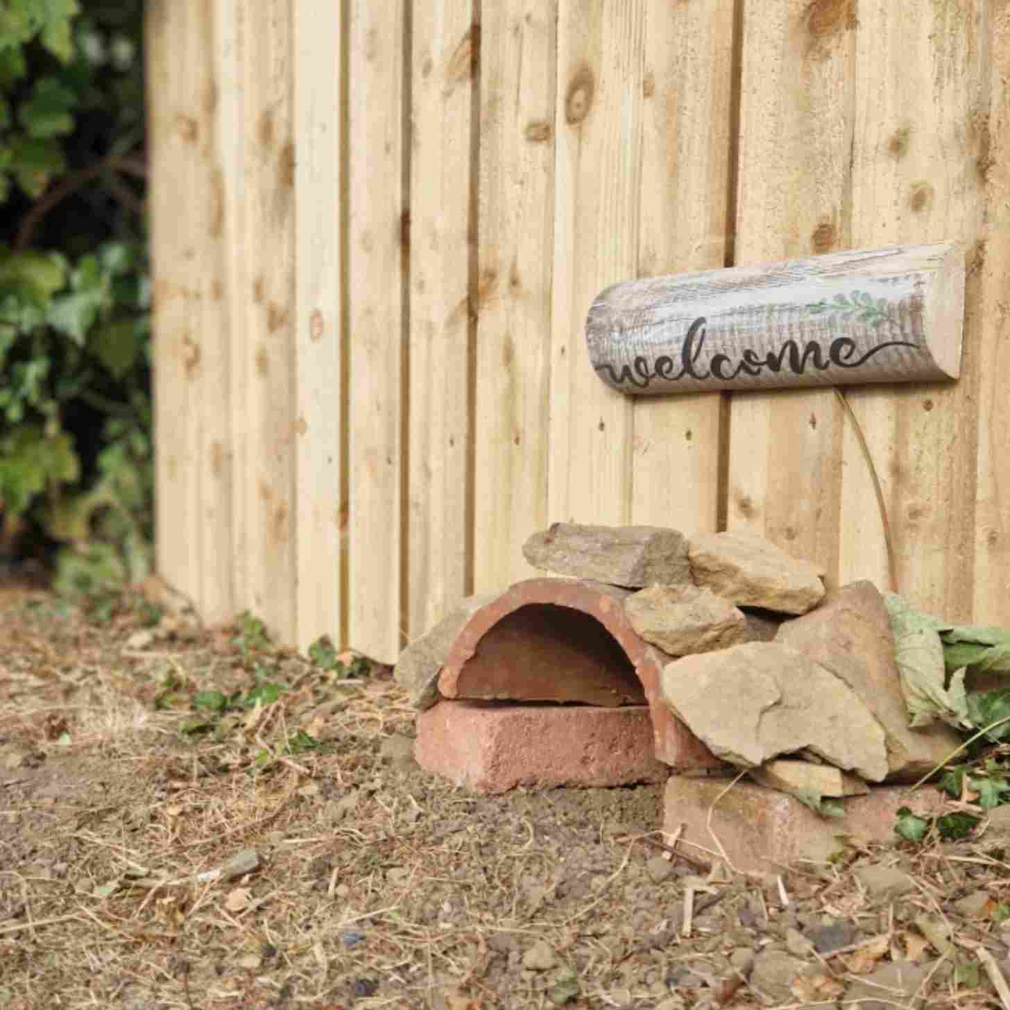 a welcome sign above a hole in a fence