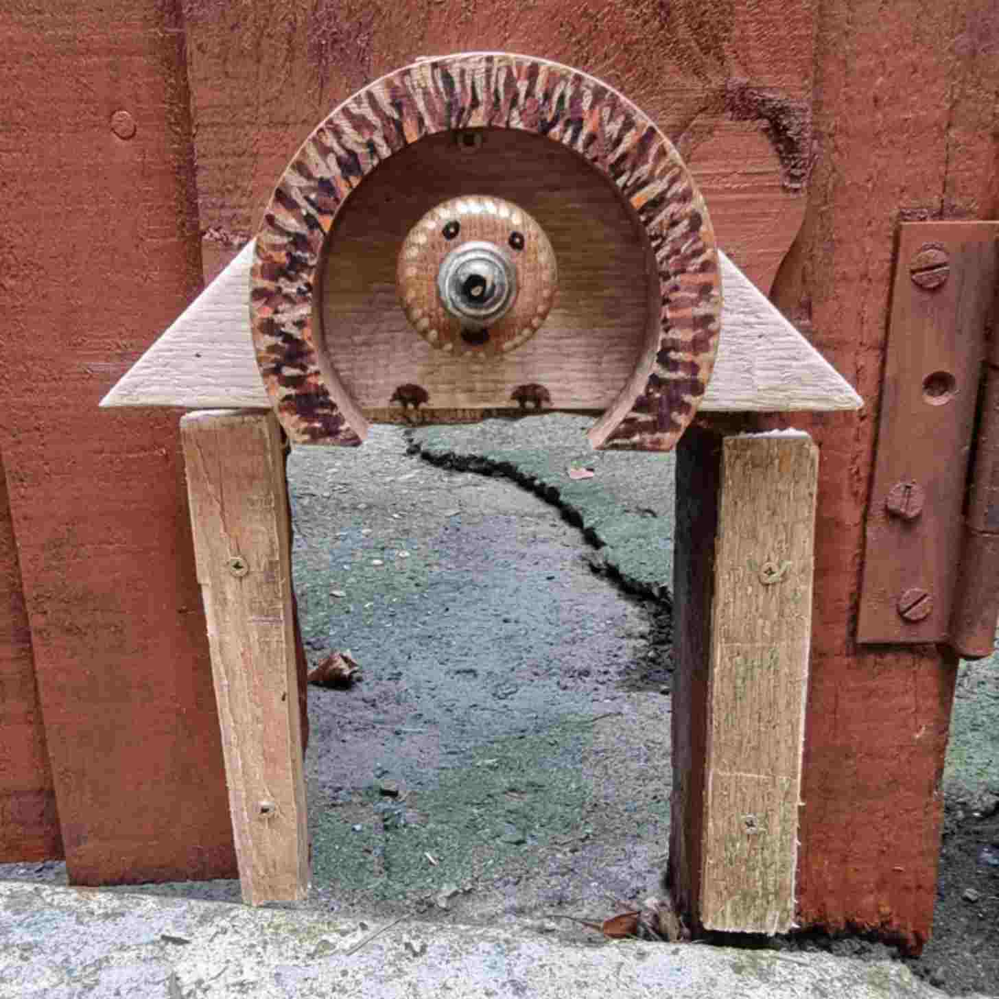 A hole in a fence with a wooden art feature that resembles a hedgehog above it