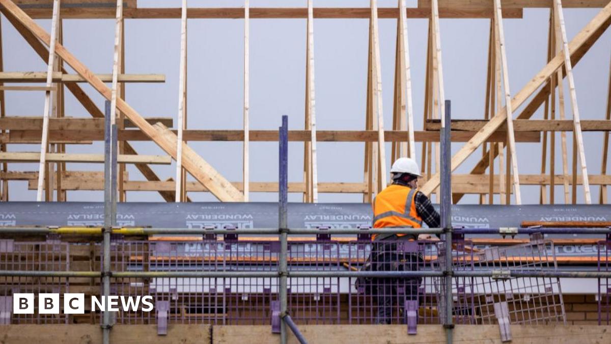 A smiling Steve Reed in suit and tie waves, wearing a red baseball cap embroidered with the words "Build Baby Build!"