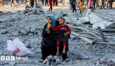 A woman child sit among grey rubble, pensively.