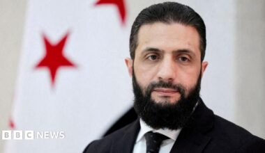 Syrian President Ahmed al-Sharaa waves amid a crowd of people