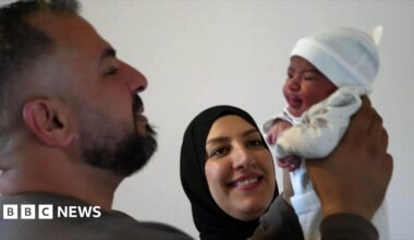 Ahmed with his wife, Nour and teenage daughter, Rahaf. They are all happy and focused on a sleeping newborn baby, being held by Ahmed and wrapped in a cream coloured blanket.