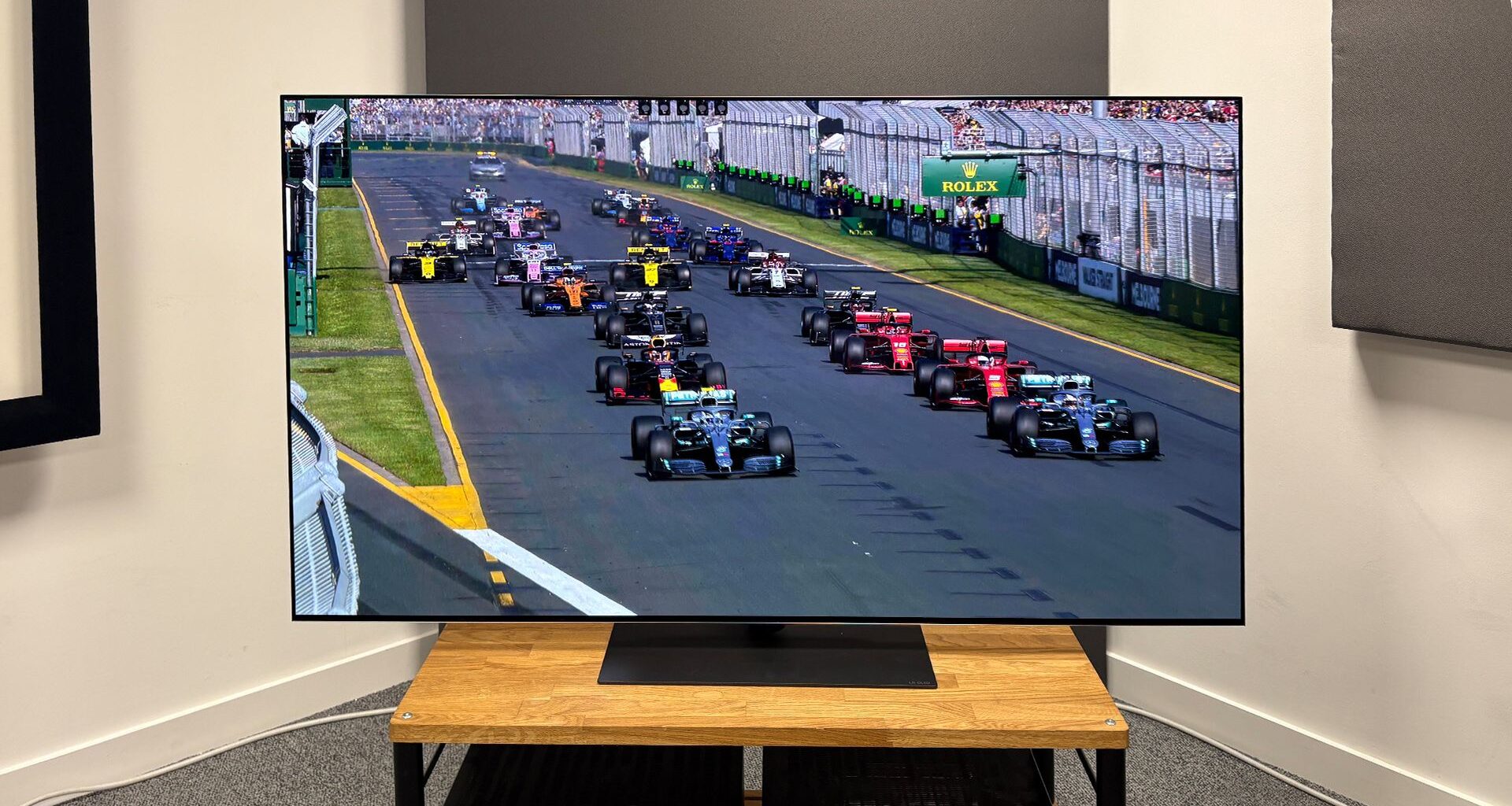The 65-inch LG G5 OLED TV pictured on a wooden rack. On the screen is a still from Netflix F1 series Drive to Survive.