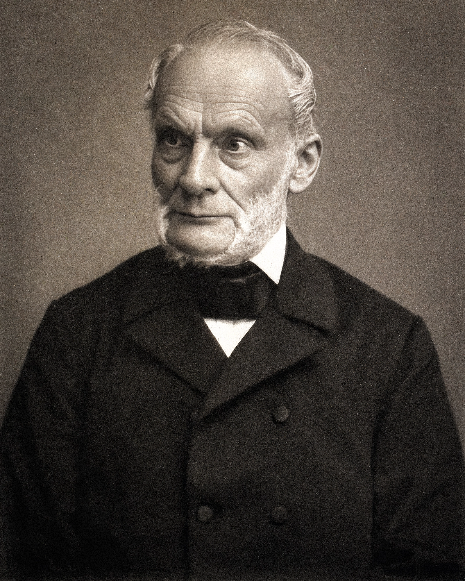 A black-and-white photo of a man in a dark suit with a white beard.